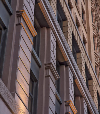 kraemer-design-group-kdg-detroit-1212-griswold-exterior-close-up-cornices-structure-architecture-building-dark-brown-lit-windows-header